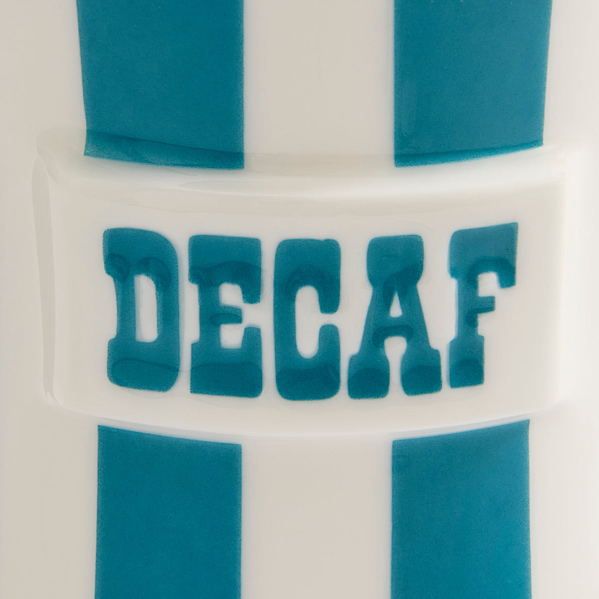 Close-up of a white cylindrical product with blue vertical stripes and the word 'DECAF' in raised blue letters across the center.