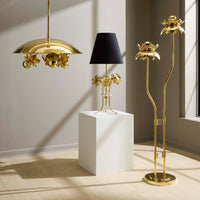 Gold floral-themed lamps and a black lampshade on a white cube in a room with sunlight casting shadows.