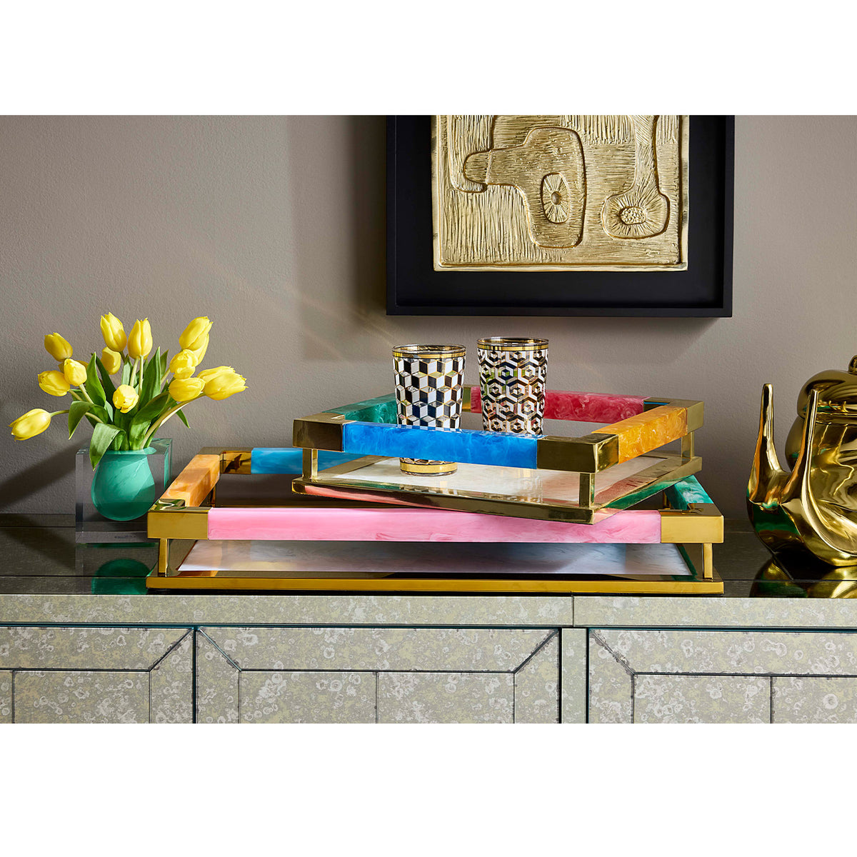 Decorative tray with colorful trays on a shelf, yellow tulips, and abstract art in the background.