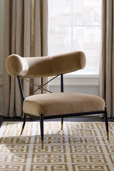 Beige velvet accent chair with black and brass feet in front of window