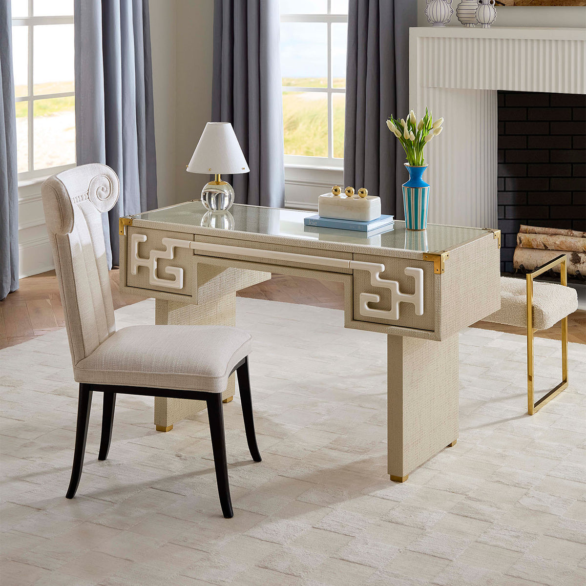 Beige desk with decorative elements in a room with large windows and a fireplace.