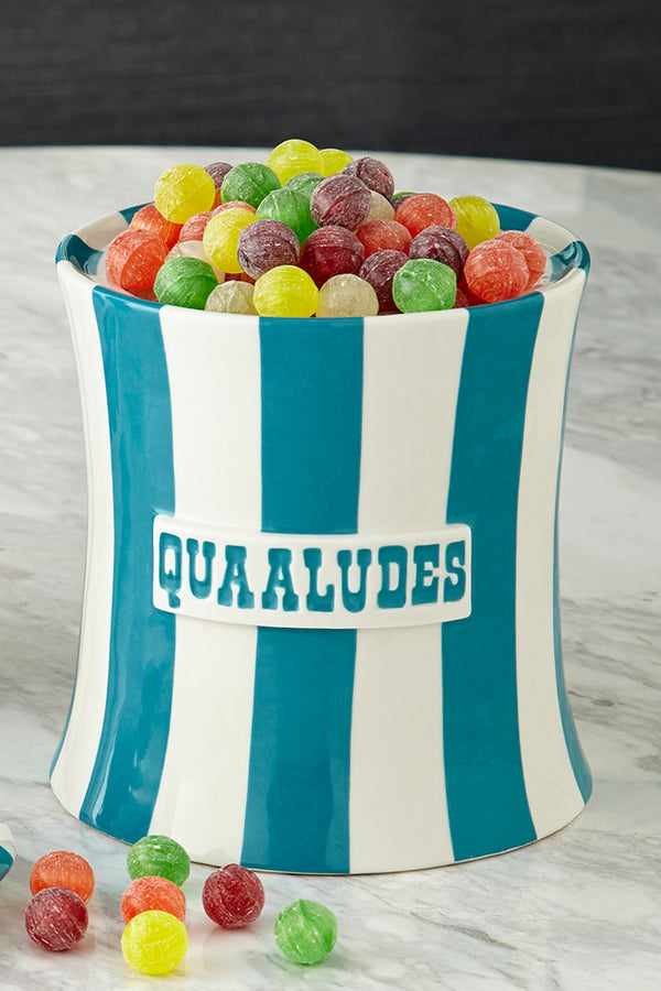 A tall ceramic candy bin with vertical teal and white stripes, filled with colorful round candies. The front has a white label with the word 'QUAAALUES' in teal.