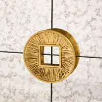 Gold circular light fixture with textured design on a marble wall background