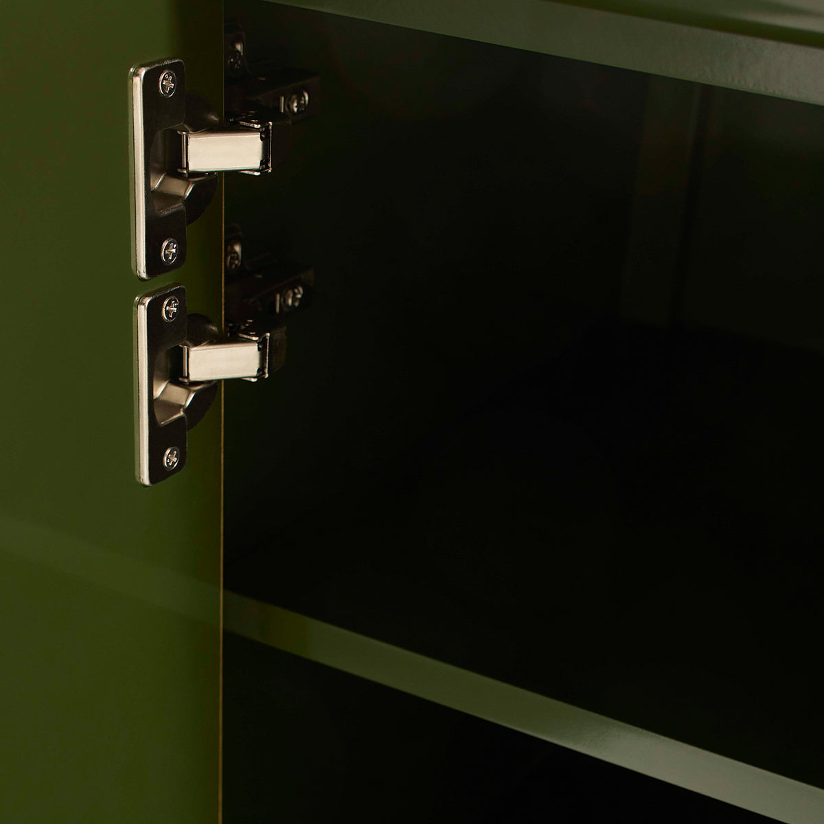 Close-up of a metallic cabinet hinge on a green cabinet door.