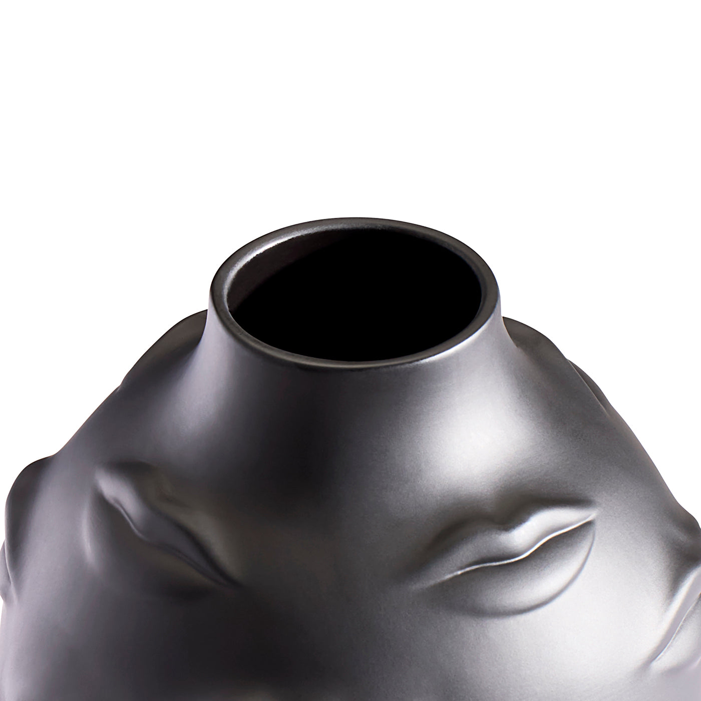 Close-up of a sculptural metallic vase or vessel with a wide circular opening, featuring embossed facial features including closed eyes and lips, in a dark silver finish against a white background.