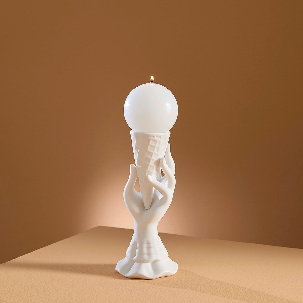 White ceramic sculpture of a hand holding a light bulb against a brown background