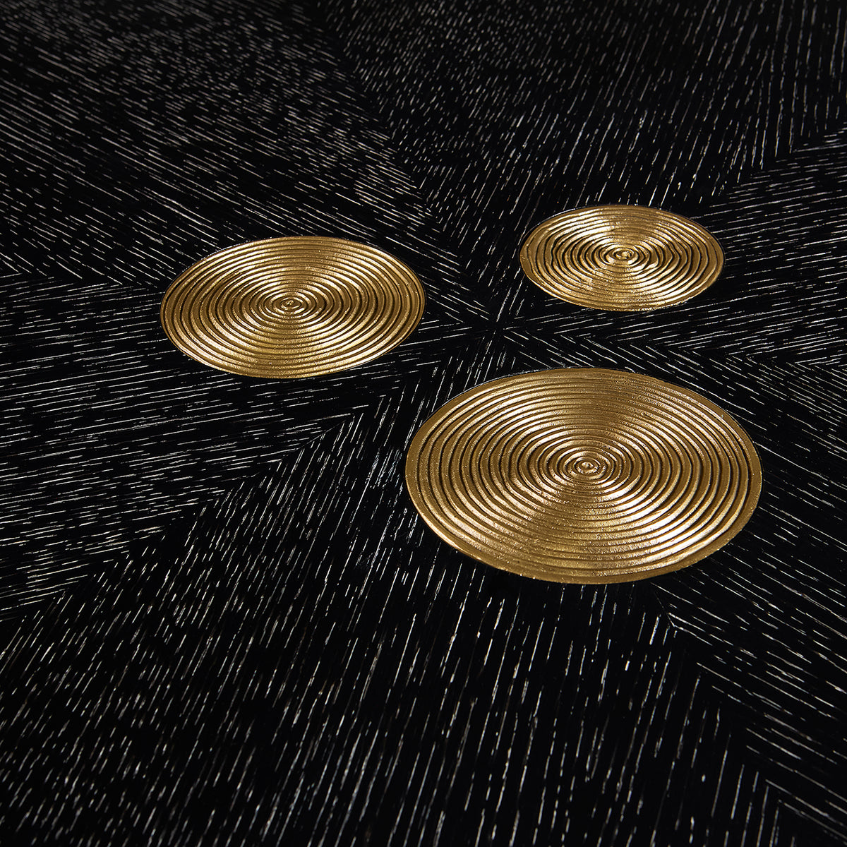 Three gold circular coasters on a black textured surface