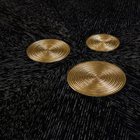 Three gold circular coasters on a black textured surface