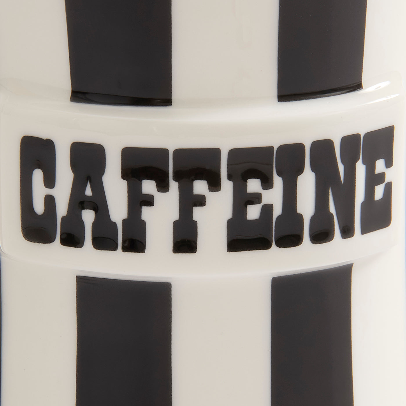 Close-up of a white cylindrical product with bold black vertical stripes and the word 'CAFFEINE' in large black letters across the center.