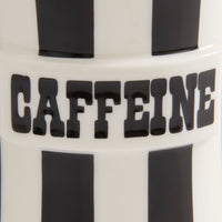 Close-up of a white cylindrical product with bold black vertical stripes and the word 'CAFFEINE' in large black letters across the center.